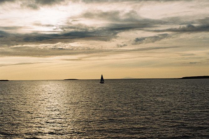 夕阳西下,一艘远航而归的渔船从海平面缓缓向岸边靠近,好一番孤帆远影