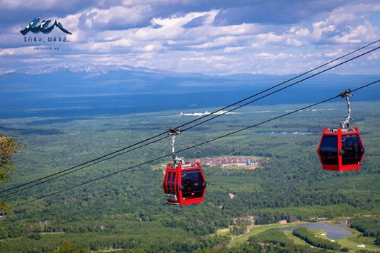 红色的缆车在蓝天和绿色中显得格外的明亮,与远处的长白山遥相呼应